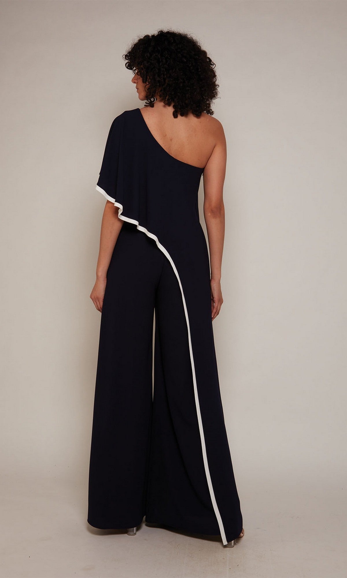 A person wearing the Long Formal Jumpsuit: Alyce 70049, a black one-shoulder style with white trim, stands facing away against a plain background.